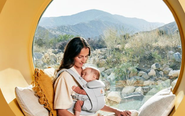 Image of mother sitting by a round window with her baby in the baby carrier.