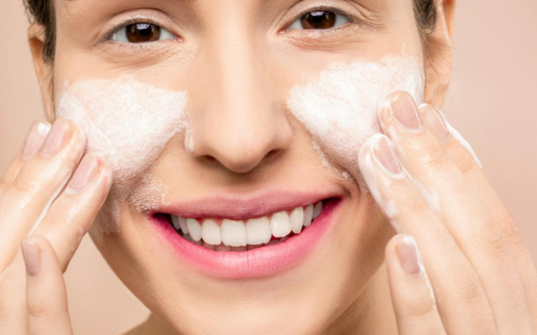 Image of a woman applying cleanser on her face while smiling