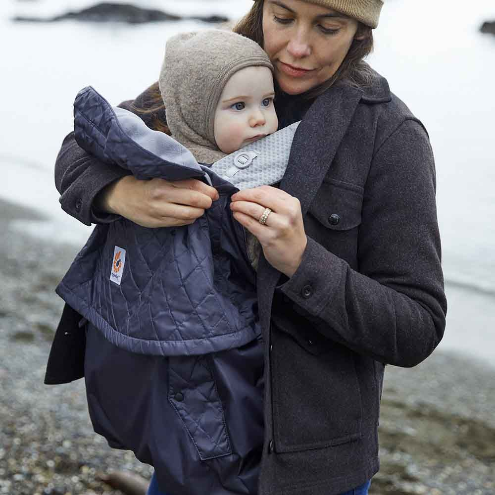 Image of a baby carrier with various accessories, such as a sunshade or weather cover, being used outdoors.