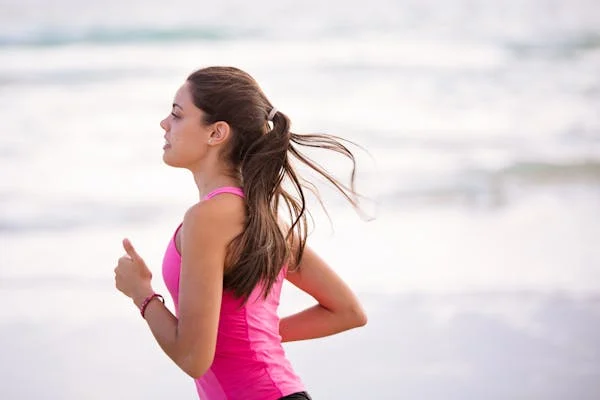 A girl running along the ocean. She is wearing a pink shirt.