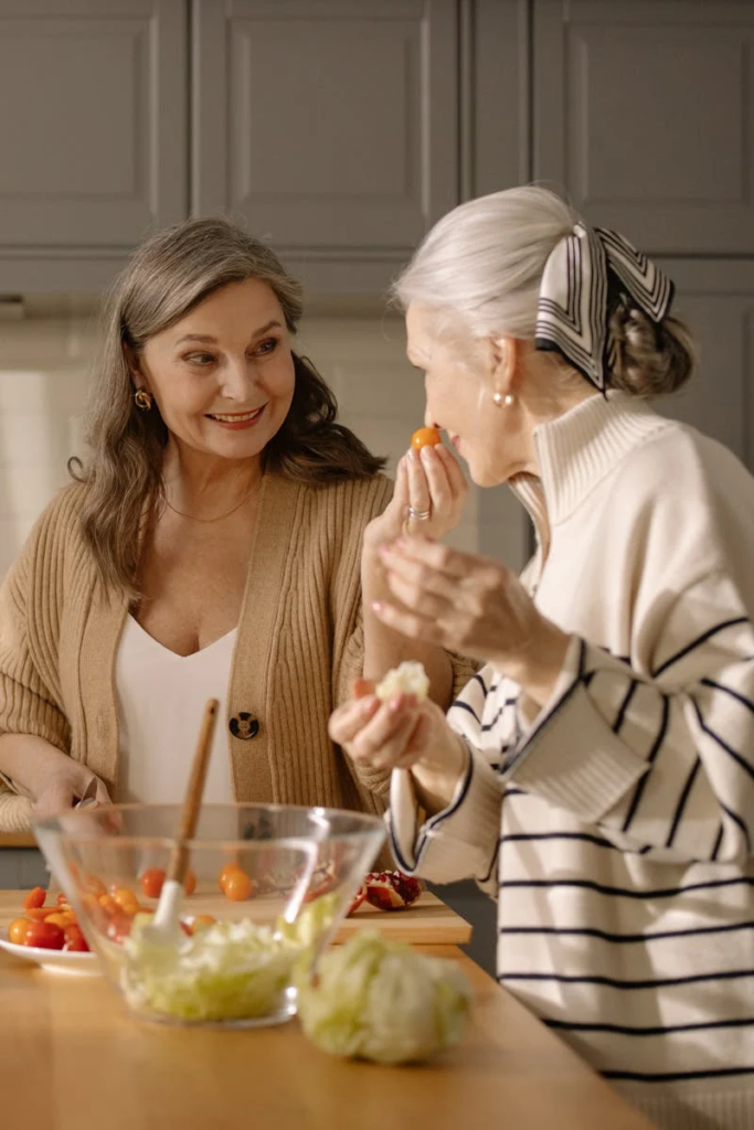 Image of 2 elderly women preparing and smelling food.